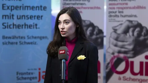 Frau spricht vor Mikrofon vor politischen Plakaten.