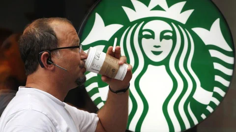 Mann trinkt Kaffee aus Becker vor Starbuckslogo