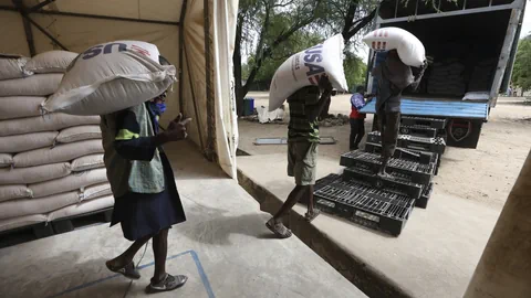 Männer tragen Säcke mit Korn, USAID steht drauf.