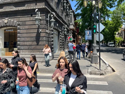 Menschen überqueren eine Strasse neben einem historischen Gebäude mit Geschäften.