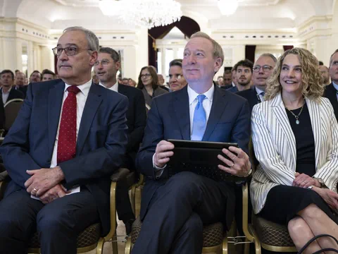 Personen in Anzügen sitzen in einem vollbesetzten Saal.