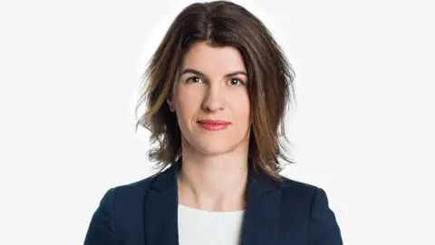 Frau mit braunem Haar im Anzug vor weissem Hintergrund.