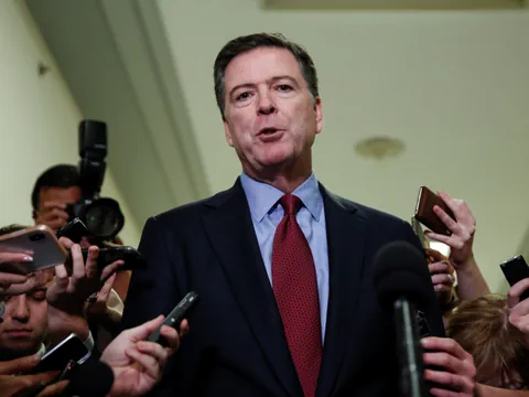 Ein Bild von James Comey, er schaut in die Kamera und ist von vielen Journalistinnen und Journalisten umgeben. 