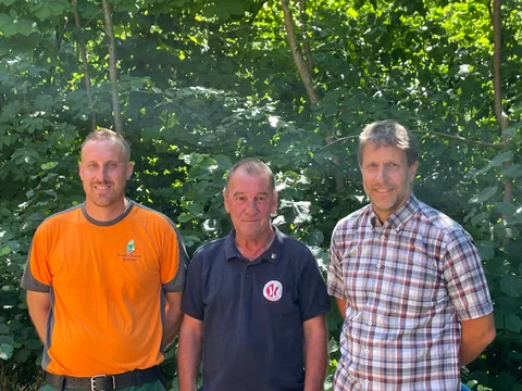 Drei Männer stehen vor einer grünen Waldkulisse.