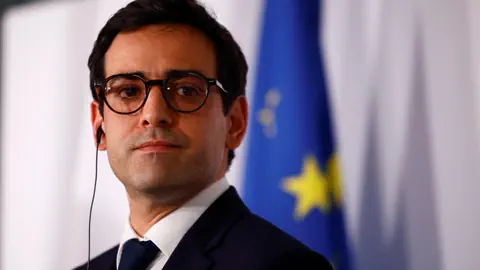 Séjourné mit Brille vor EU-Flagge.