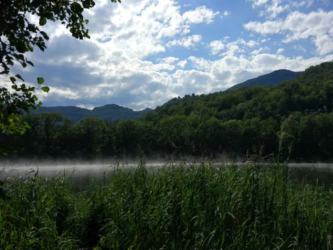 See im Hintergrund Bäume und Berge.