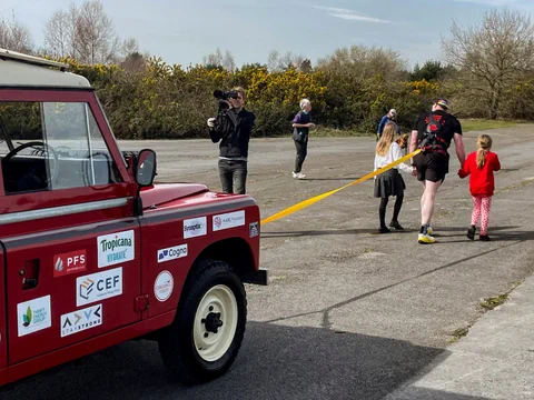 Mensch zieht Land Rover mit Seil, beobachtet von Kindern.