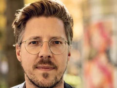 Mann mit dunkelblondem Haar, Schnurrbart und einer runden, silbernen Brille