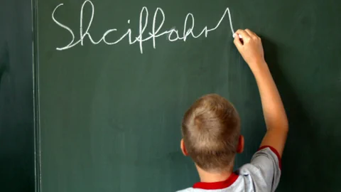 Junge schreibt 'Schifffahrt' falsch an Tafel.