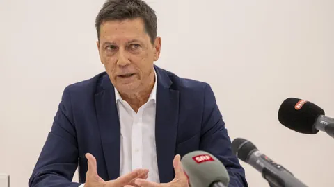 Mann in Anzug bei Pressekonferenz mit Mikrofonen.