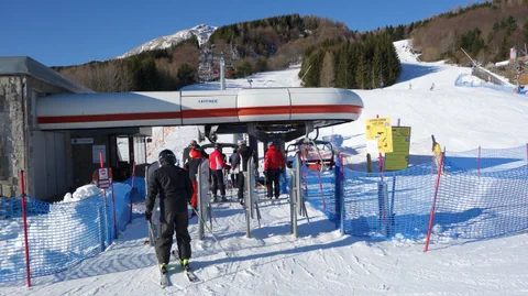 Ski- und Snowboardfahrer beim Einsteigen in den Sessellift an einer Bergstation.