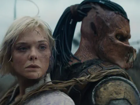 Ein Alien trägt einen kaputten Roboter auf dem Rücken.