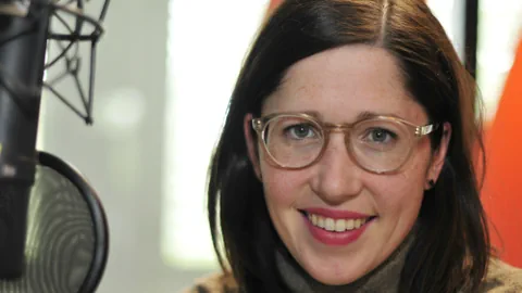 Frau mit Brille und Mikrofon im Studio.