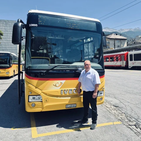 Mann steht vor einem gelben Bus auf einem Parkplatz.