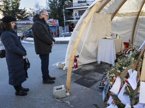 Zwei Personen stehen vor einem Gedenkzelt mit Blumen und Kerzen.