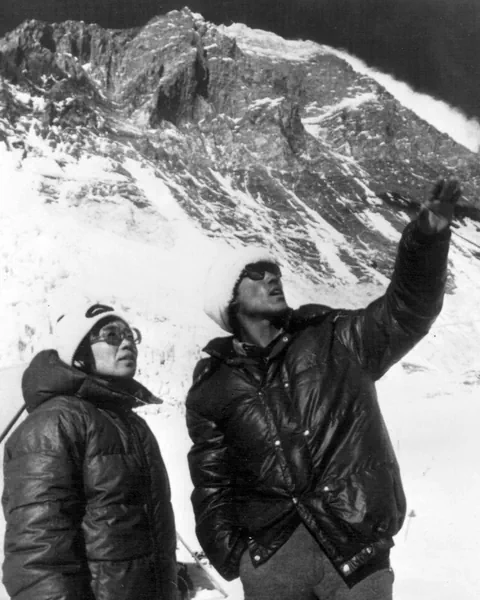 Zwei Männer in dicker Kleidung vor schneebedecktem Berg.