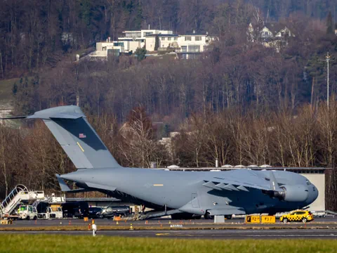 Militärflugzeug auf dem Rollfeld vor bewaldetem Hügel.