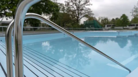 Leeres Schwimmbecken im Freien mit Metallgeländer.