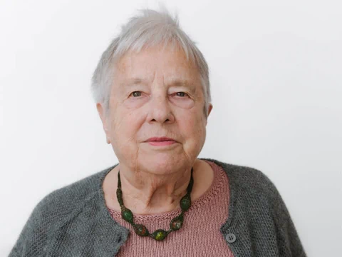 Frau mit kurzen grauen Haaren, Halskette und Wolljäckchen.