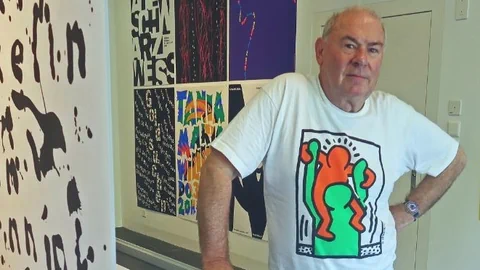 Ein Mann in bunten Shirt vor farbigen Plakaten.