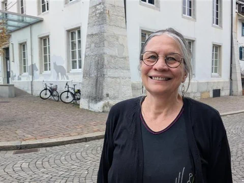 Lächelnde Frau auf gepflasterter Strasse vor einem Gebäude.