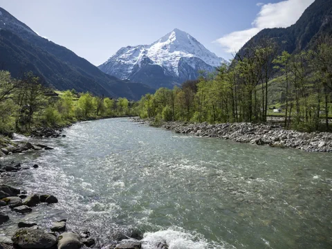 Fluss vor schneebedecktem Berg und bewaldeten Hügeln.