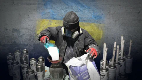 Mann in Winterkleidung und Gasmaske füllt weisses Pulver in ein Gefäss. Hintergrund Betonwand mit Ukraineflagge