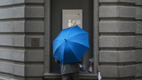 Ein Kunde mit Regenschirm an einem Bancomat der Credit Suisse.