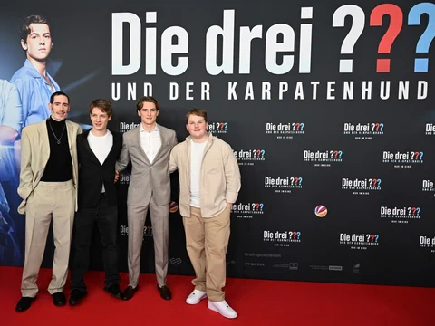 Vier Personen posieren auf rotem Teppich vor 'Die drei ???'-Plakatwand.