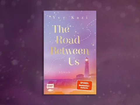 Buchcover mit Leuchtturm in einer Landschaft bei Sonnenuntergang und dem Titel 'The Road Between Us'.