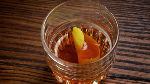 Whiskyglas mit bernsteinfarbener Flüssigkeit und Zitronenschale