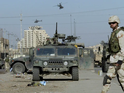 Soldaten und militärische Fahrzeuge in städtischem Gebiet mit Helikoptern am Himmel.