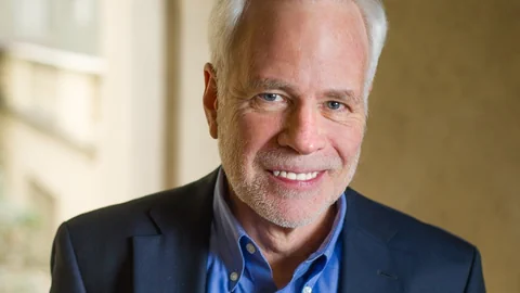 Mann mit hoher Stirn und weissen Haaren lächelt in die Kamera.