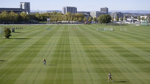 Grosse Rasenfläche, eine Frau joggt im Vordergrund, eine Spaziergängerin und Fussballtore