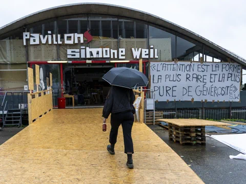 Person mit Regenschirm betritt Pavillon Simone Weil bei Regen.