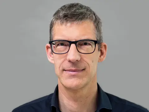 Mann mit Brille vor grauem Hintergrund.