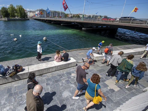 Menschen spazieren an einem Wasserufer mit Brücke und Fahnen.