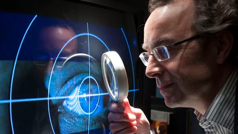 Ein Mann blickt durch eine Lupe auf einen Schirm, auf dem das Tatort-Logo zu sehen ist - das Auge in einem Fadenkreuz.