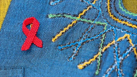 Rote Schleifenbrosche auf blauem Stoff mit bunten Nähten.