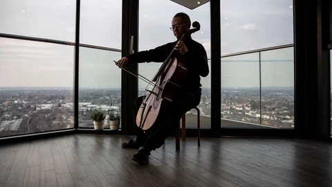 Ein Mann spielt Cello, hinter ihm die Aussicht über eine Stadt.