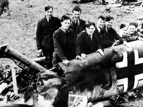 Gruppe Männer posieren mit Flugzeugwrack und deutscher Markierung.
