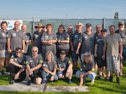 Gruppe von Menschen in grauen Hemden posieren draussen auf Gras.