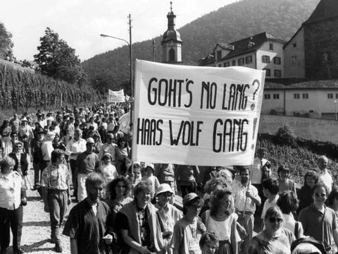 Menschenmenge bei einem Protest mit einem grossen Banner in einem Dorf.