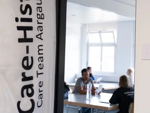 Mehrere Personen sitzen an einem Tisch in einem Büro oder Besprechungsraum.