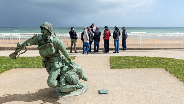 Reisegruppe vor einem Soldatendenkmal in der Normandie.