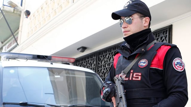 Türkischer Polizist mit Maschinenpistole steht Wache vor einem Haus, hinter ihm ein Polizeifahrzeug Türkischer Polizist mit Maschinenpistole steht Wache vor einem Haus, hinter ihm ein Polizeifahrzeug