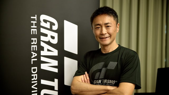 Kazunori Yamauchi posiert vor einem Gran-Turismo-Plakat.