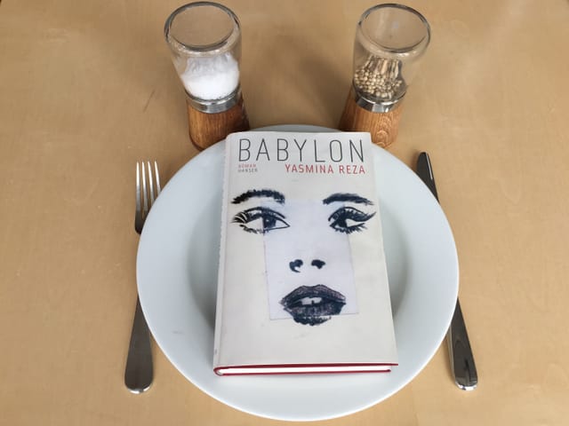 Der Roman «Babylon» von Yasmina Reza liegt auf einem weissen Teller, Messer und Gabel daneben. Oberhalb steht eine Pfeffer- und Salzmühle Der Roman «Babylon» von Yasmina Reza liegt auf einem weissen Teller, Messer und Gabel daneben. Oberhalb steht eine Pfeffer- und Salzmühle