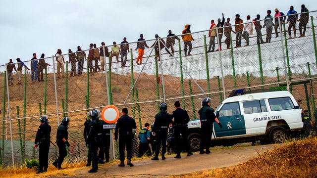 Die Guarda Civil warten unten, die Flüchtlinge sind oben auf dem Zaun. Die Guarda Civil warten unten, die Flüchtlinge sind oben auf dem Zaun.