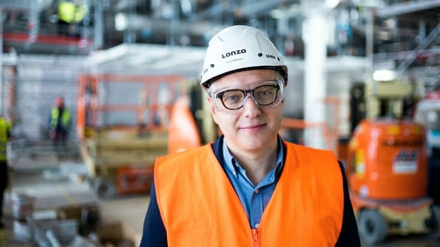 Ein Mann mit Helm und Leuchtweste steht in einer Fabrikhalle. Ein Mann mit Helm und Leuchtweste steht in einer Fabrikhalle.